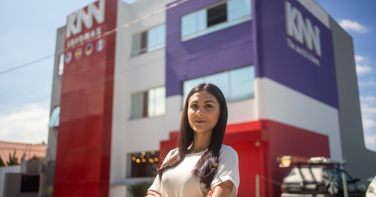 Uma mulher de cabelos pretos e compridos em frente a escola da KNN Idiomas Balneário Camboriú.