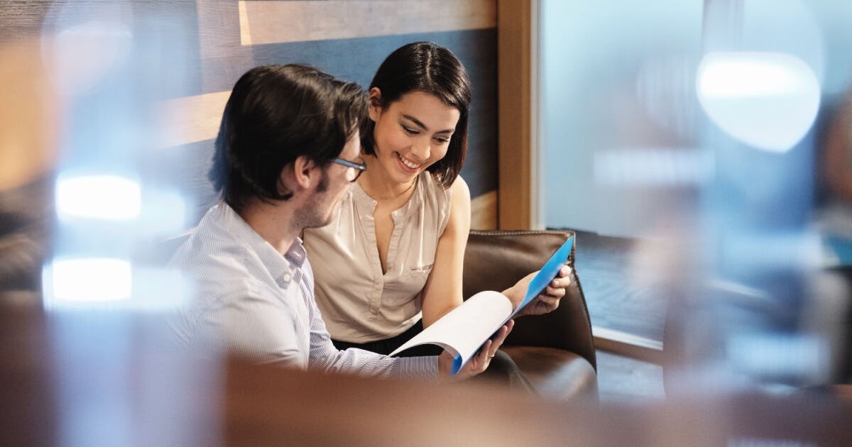 Um homem e uma mulher sentados em um sofá, observando atentamente um laptop.