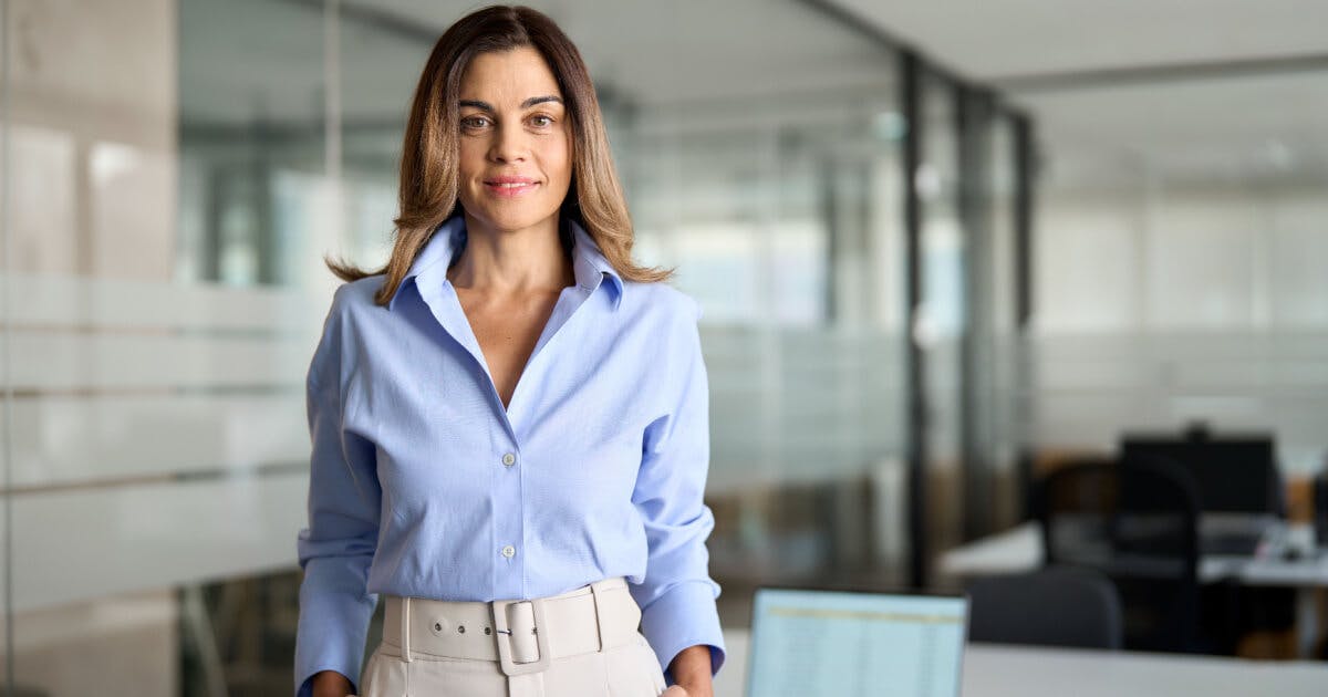 Uma mulher com camisa azul e calças brancas está em pé em um escritório.