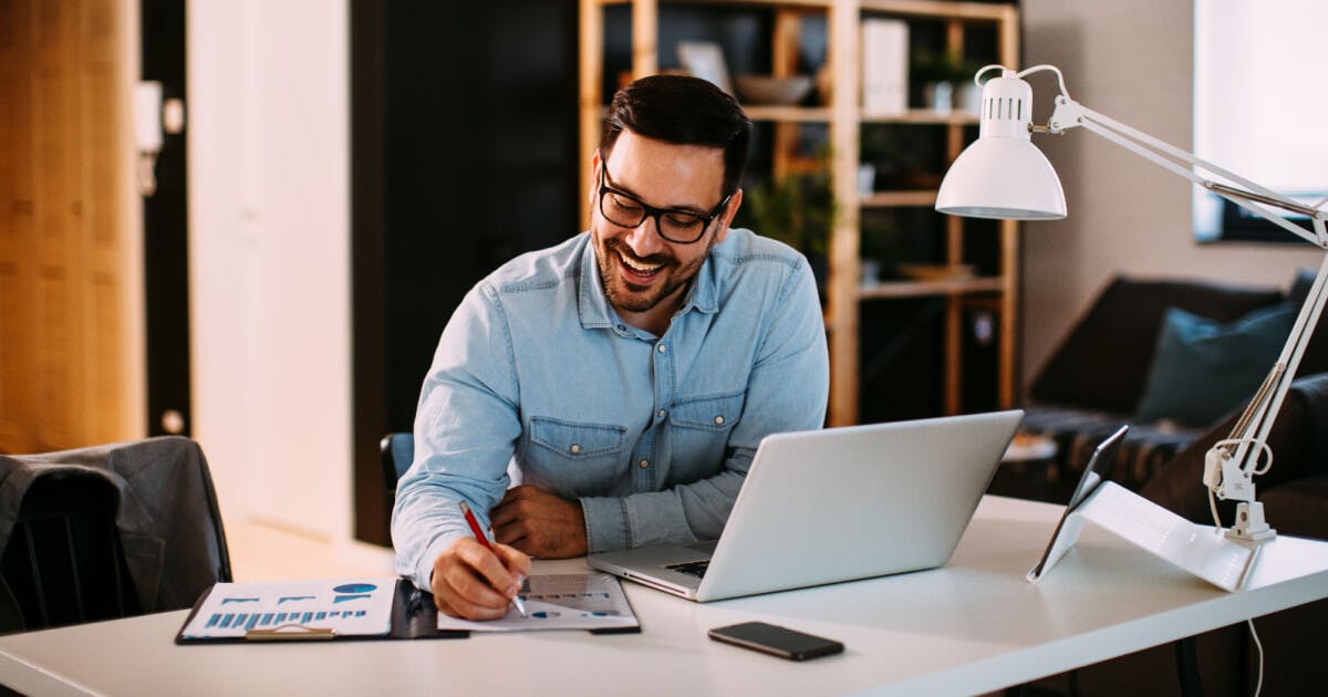 Um homem sentado à mesa, utilizando um laptop e segurando uma caneta.