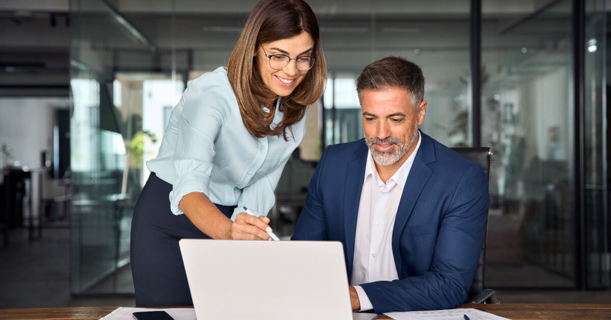 Um homem e uma mulher colaboram em um laptop, concentrados em suas tarefas.