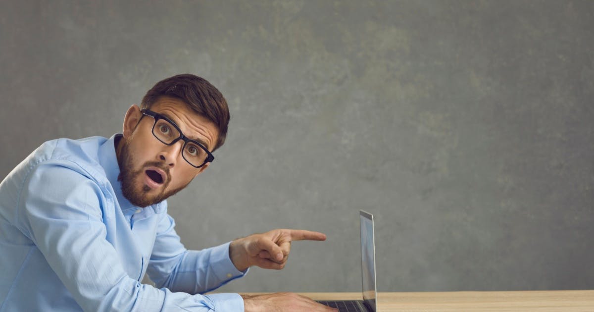 Homem de óculos, com uma expressão de surpresa apontando o dedo para o notebook e olhando para você.