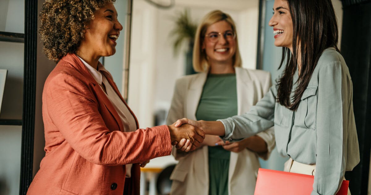 Duas mulheres apertando as mãos em um ambiente de escritório, simbolizando um acordo ou colaboração profissional.