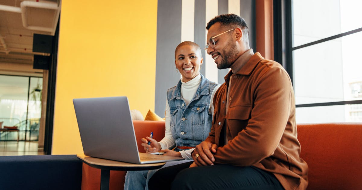 Um homem e uma mulher sentados em um sofá, utilizando um laptop juntos.