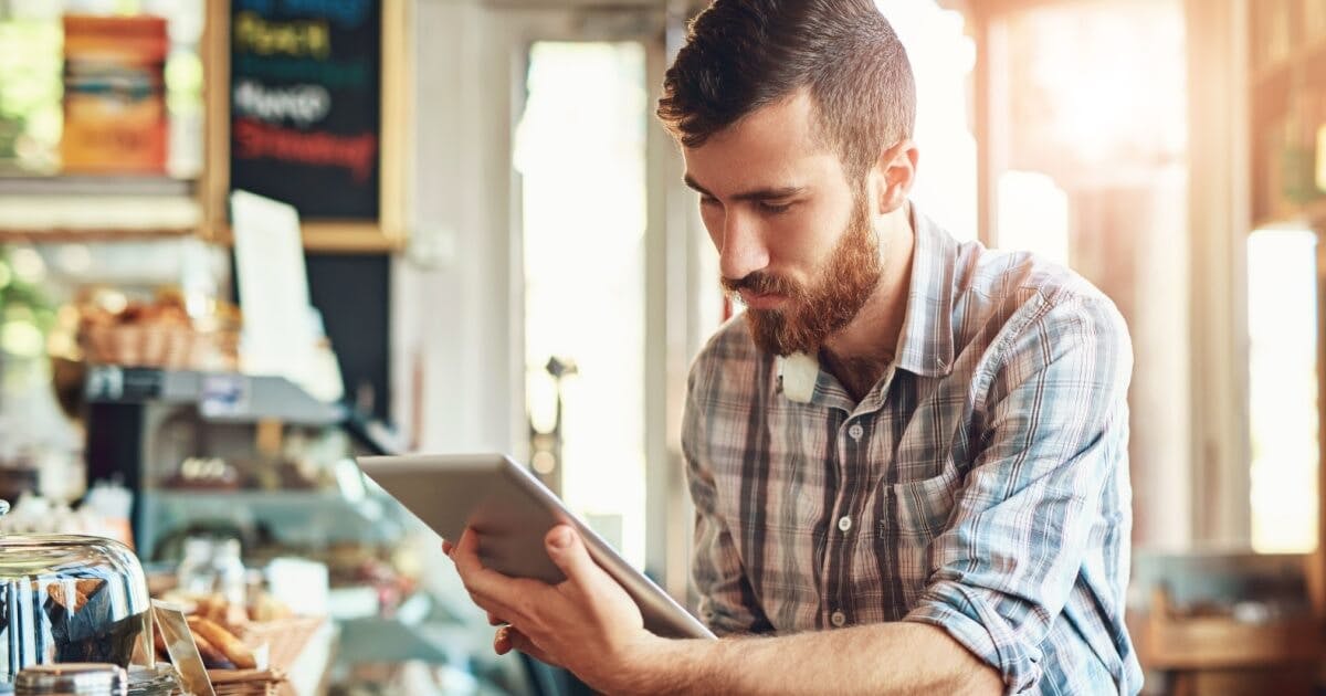 Homem com tablet na mão e camiseta xadrez.