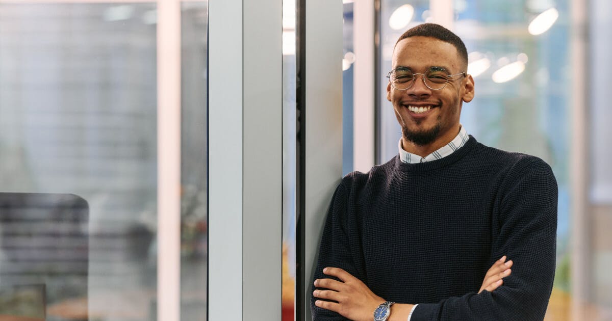 Homem sorridente em um edifício de escritórios, transmitindo uma atmosfera de positividade e profissionalismo.