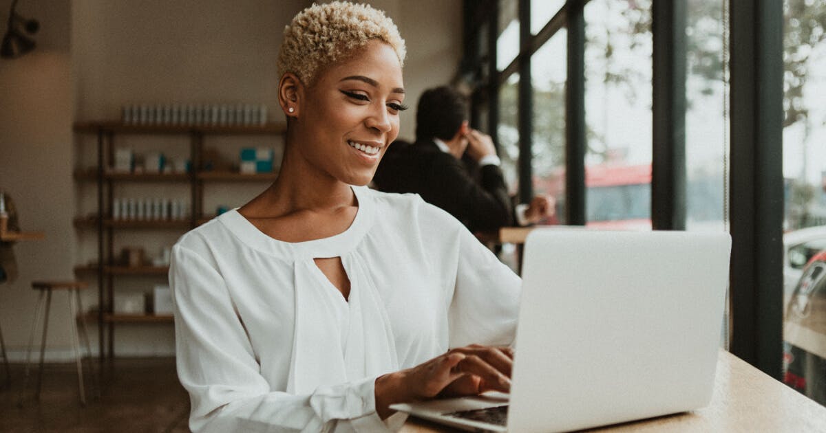 Uma mulher sorri enquanto utiliza seu laptop, transmitindo alegria e concentração em seu trabalho.