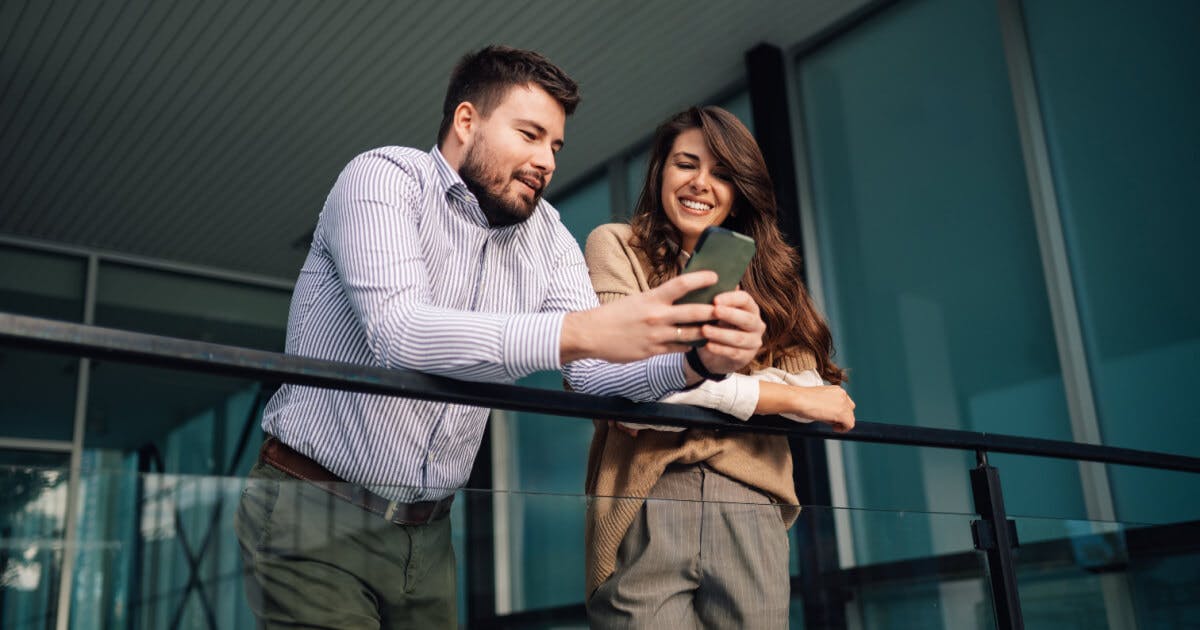 Um homem e uma mulher em um balcão, observando seus celulares com interesse e atenção.