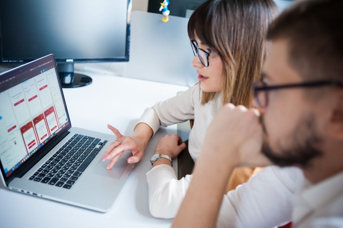 Homem e mulher usando óculos e olhando para um notebook . Ela está com a mão no touchpad.