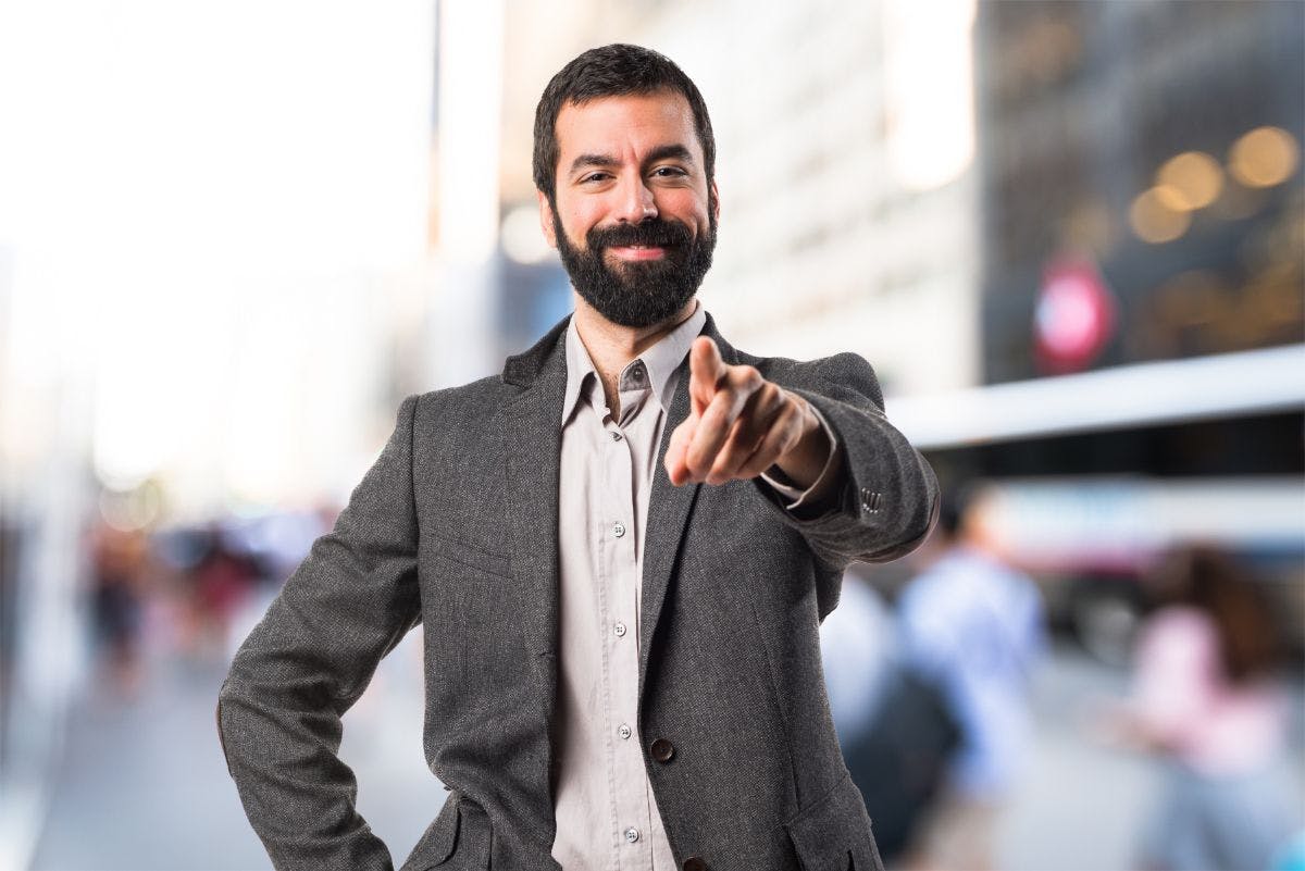 Homem de terno com expressão feliz apontando o dedo para a câmera.