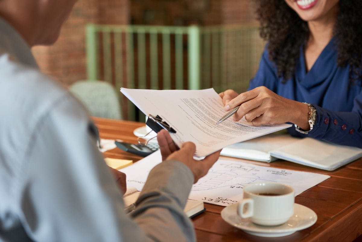 Duas pessoas trocando um contrato e um café em cima da mesa.