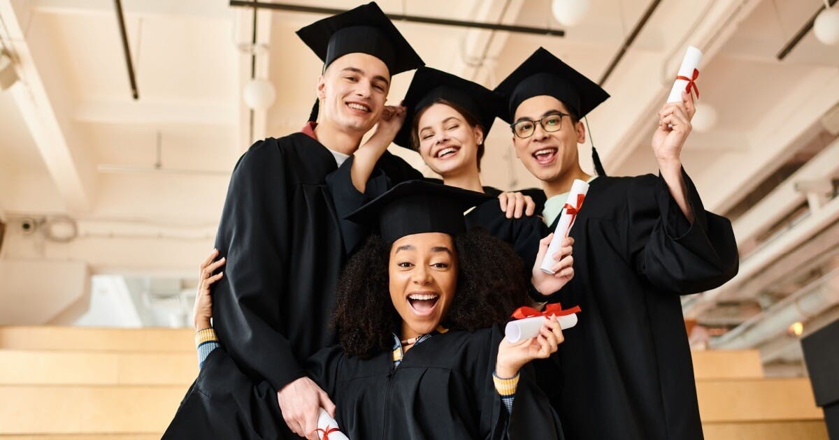 Quatro alunos com toga de formatura e canudos sorrindo.