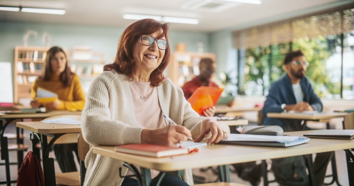 Alunos mais velhos dentro de uma sala de aula com livros na mesa.