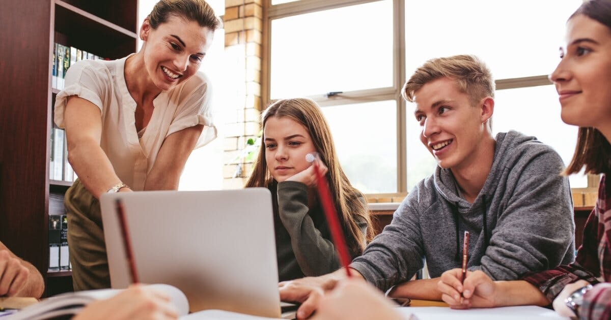 Professora orientando três alunos olhando para um notebook.