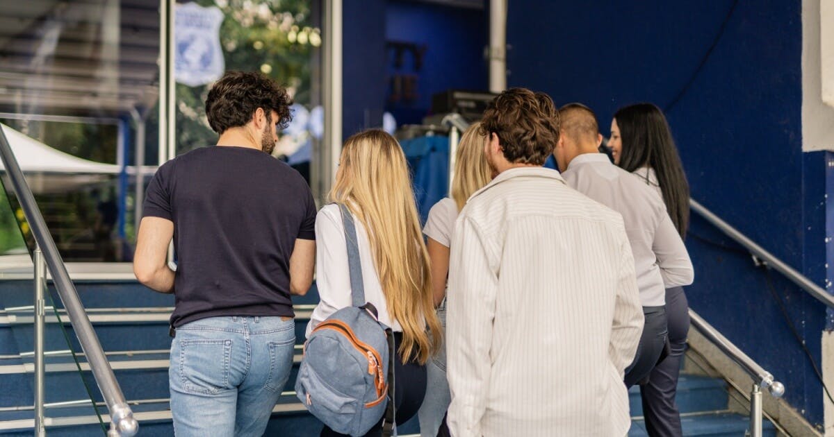 Alunos de costas subindo em uma escadaria de uma escola.