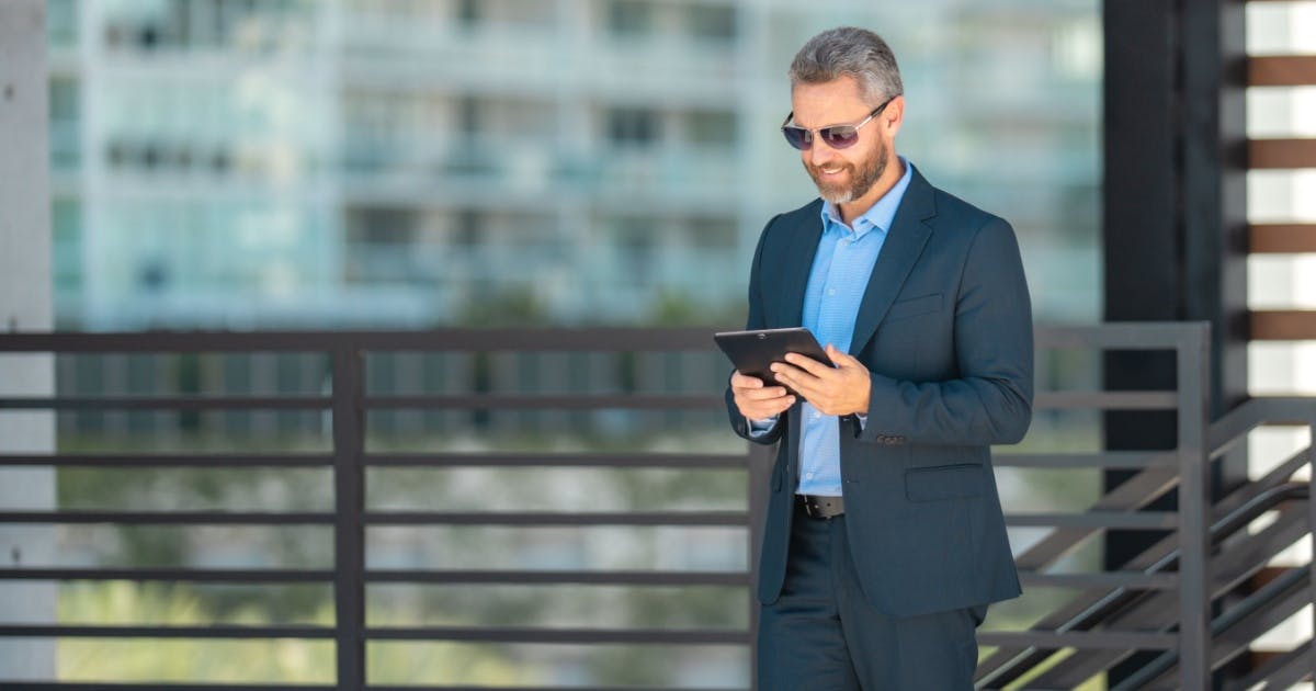 Homem de terno, óculos, sorrindo e com um celular na mão.
