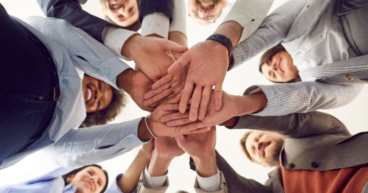 Diversas pessoas com as mãos juntas no meio. A imagem é de baixo para cima.