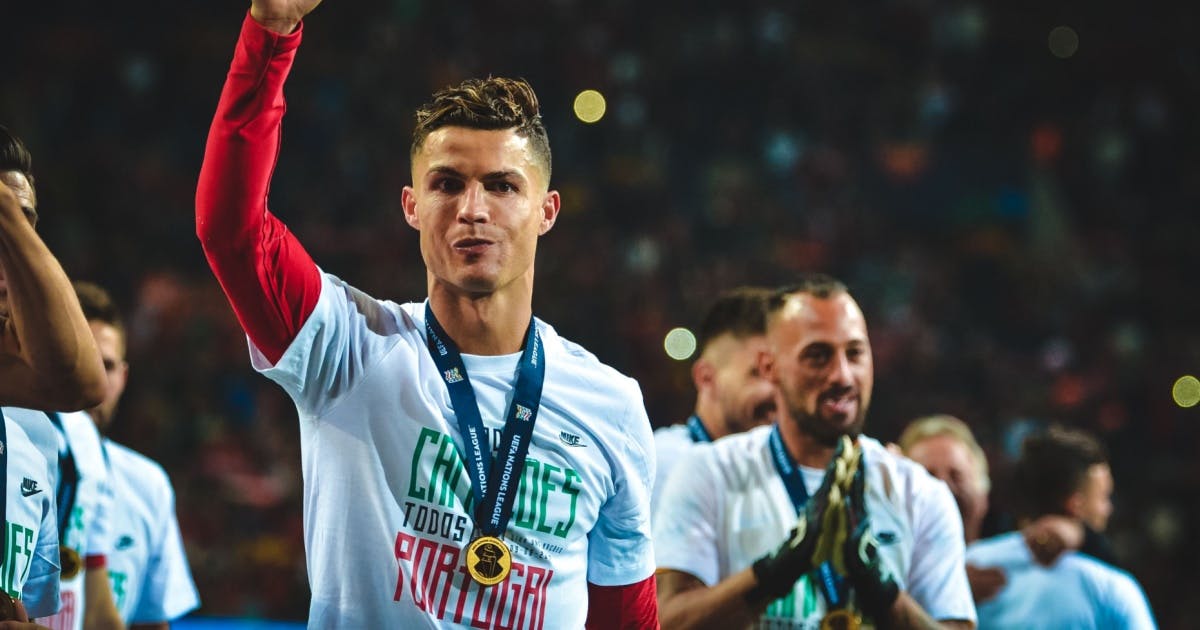 Foto do jogador português Cristiano Ronaldo comemorando com seus companheiros. Eles estão com medalhas no pescoço.