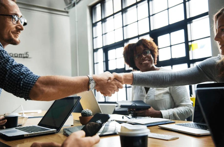 Reunião de negócios com pessoas apertando as mãos, simbolizando parceria, colaboração e sucesso em um ambiente de trabalho moderno e inspirado em inovação.