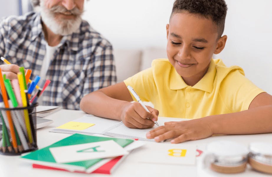 Criança feliz aprendendo na escola com ajuda de um professor idoso, promovendo inclusão e diversidade na educação.