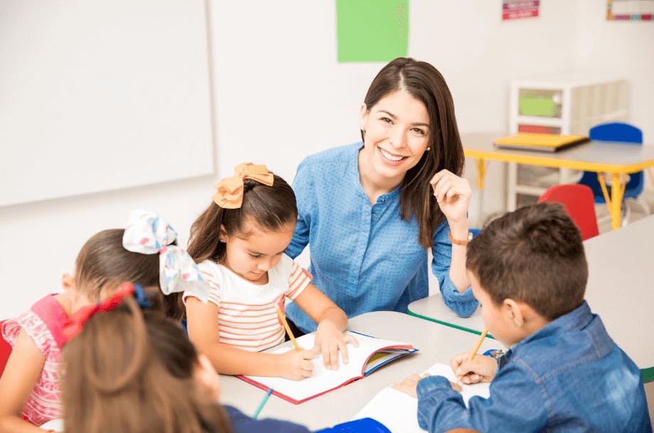 Professora sorridente interagindo com crianças em sala de aula, promovendo educação infantil e aprendizado.