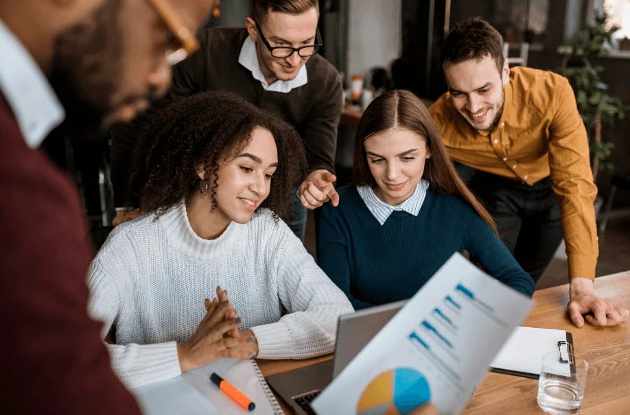 Grupo de jovens profissionais reunidos em escritório, analisando gráficos e discutindo estratégias de negócios, promovendo inovação e trabalho em equipe.