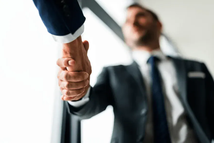 Imagem de aperto de mãos entre dois empresários de terno, simbolizando acordo ou parceria de negócios.