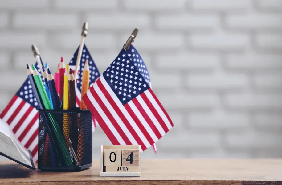 Lápis de cor, bandeiras dos EUA e calendário indicando o dia 4 de julho, símbolo de celebração do Dia da Independência dos Estados Unidos.
