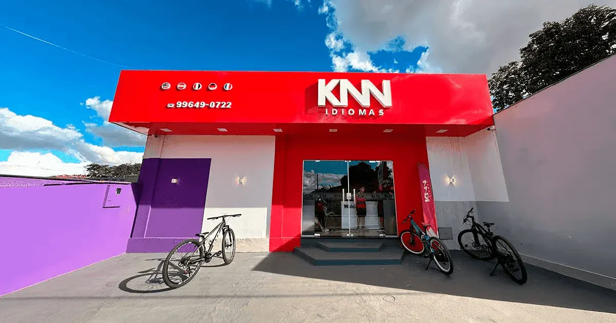 Fachada de uma escola de idiomas KNN com bicicletas na frente e céu azul ao fundo, destacando a oferta de cursos de idiomas em uma cidade moderna.