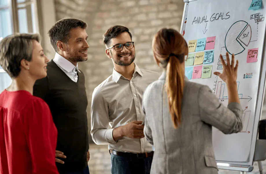 Equipe de profissionais de negócios discutindo estratégias para alcançar metas anuais, com foco em planejamento e análise de dados em reunião de trabalho.