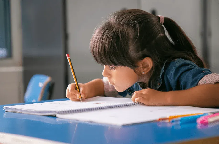 Menina estudando na escola escrevendo em caderno com concentração, ambiente de sala de aula, foco na aprendizagem e educação de crianças.