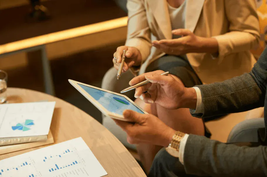 Reunião de negócios com duas pessoas analisando gráficos digitais em tablet e papel, em ambiente profissional, focando em colaboração e estratégias.