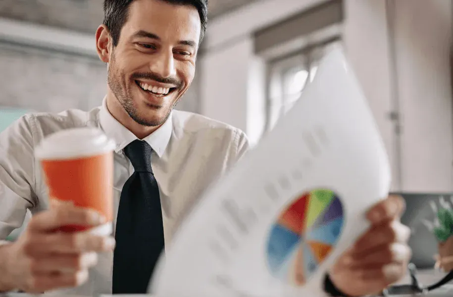 Homem de negócios sorridente segurando um copo de café e analisando gráficos em uma reunião no escritório.