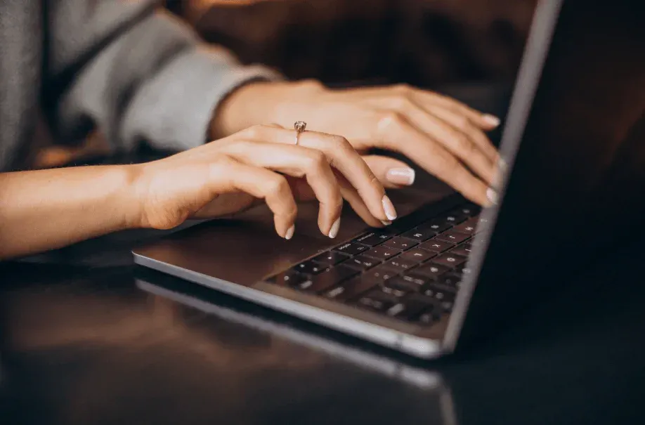 Pessoa digitando em um teclado de laptop com foco nas mãos e na tela.