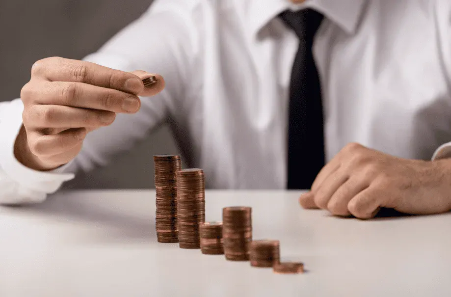 Pessoa colocando uma moeda sobre pilhas de moedas ordenadas de forma decrescente.