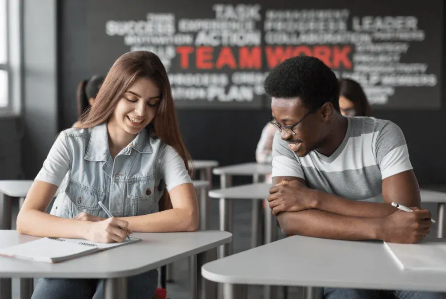 Imagem de estudantes de diferentes etnias colaborando e estudando juntos em uma sala de aula moderna, promovendo trabalho em equipe e aprendizagem colaborativa.