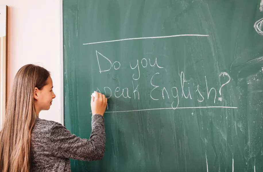  Garota escreve a frase "Do you speak English?" em um quadro-negro na sala de aula