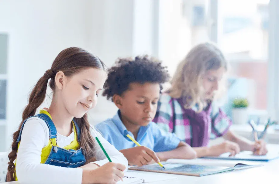 Três crianças estudando e escrevendo em sala de aula