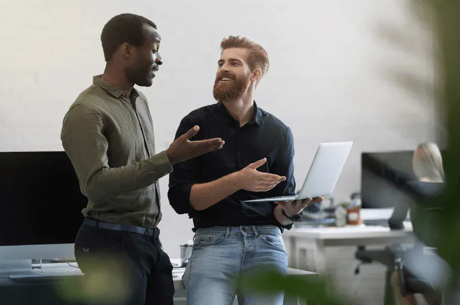 Dois homens profissionais conversando em um escritório moderno enquanto compartilham ideias usando um laptop