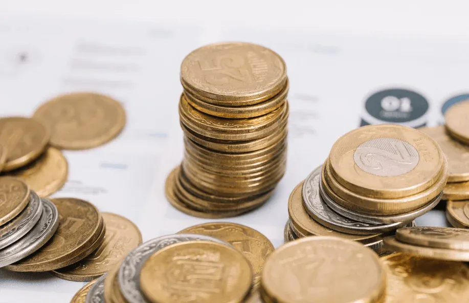 Pilha de moedas de diferentes valores sobre fundo claro, com destaque para várias moedas empilhadas, sugerindo economia, investimento e reserva financeira.