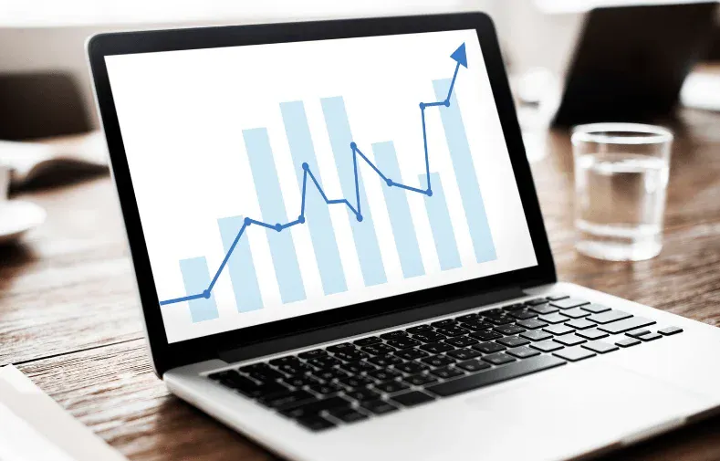 Notebook sobre uma mesa com gráfico de crescimento em azul na tela, sugerindo análise de dados, indicadores financeiros e desempenho em negócios ou investimentos.