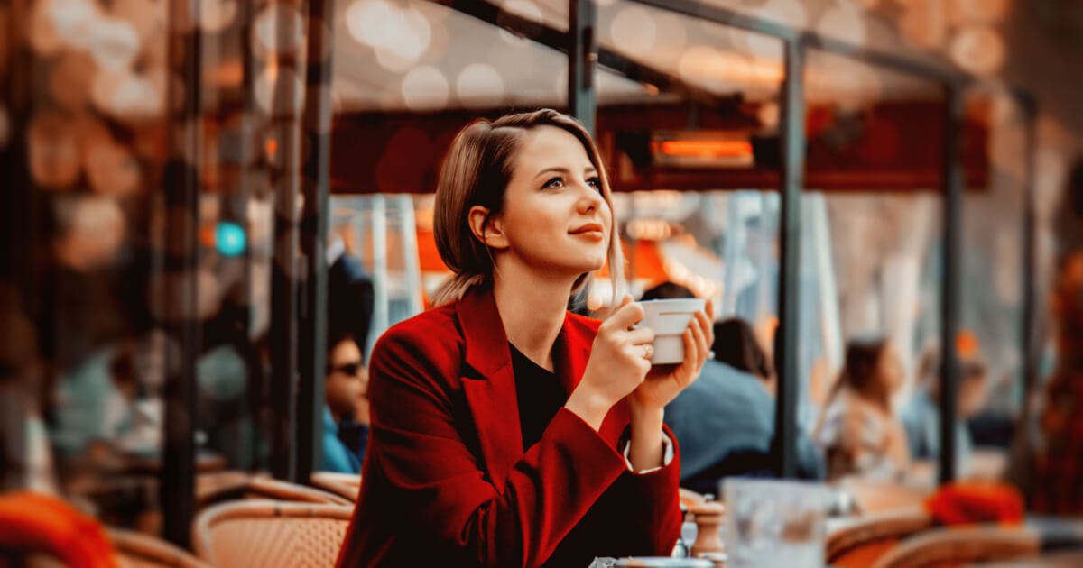 Uma mulher sentada à mesa, segurando uma xícara de café, em um ambiente acolhedor e tranquilo.