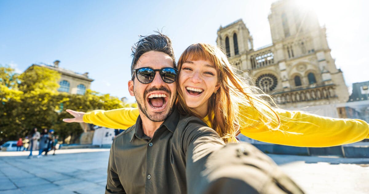 Um homem e uma mulher tirando uma selfie em frente à Catedral de Notre-Dame de Paris