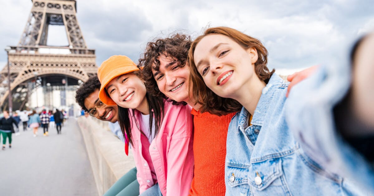 Quatro jovens tirando uma selfie em frente à Torre Eiffel, sorrindo e aproveitando o momento juntos.