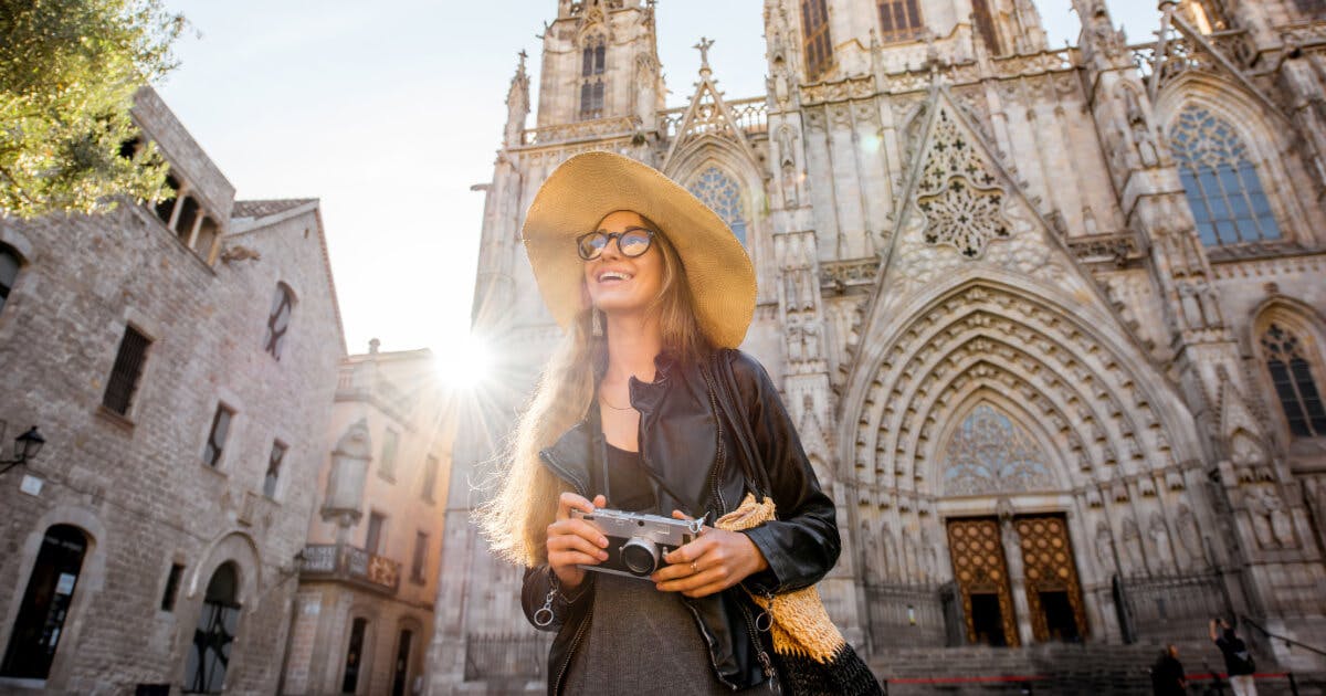 Uma mulher com chapéu e óculos de sol segurando uma câmera em frente a uma catedral.