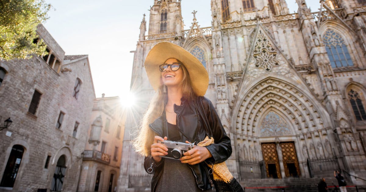 Uma mulher com chapéu e óculos de sol segurando uma câmera em frente a uma catedral.