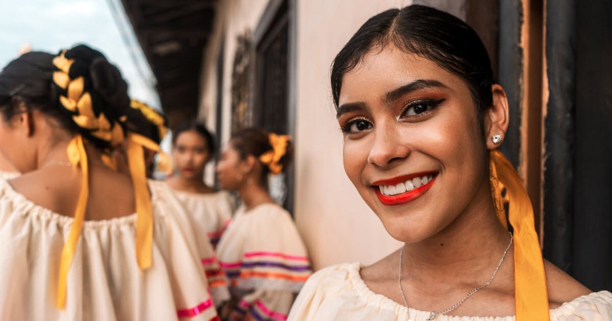 Uma mulher sorrindo, vestindo um traje tradicional mexicano colorido e elegante.