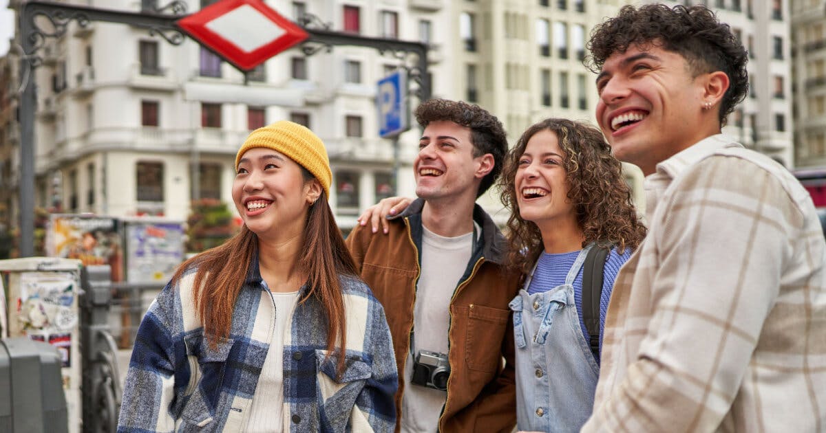 Três jovens sorrindo e posando em frente a uma cidade, transmitindo alegria e camaradagem.