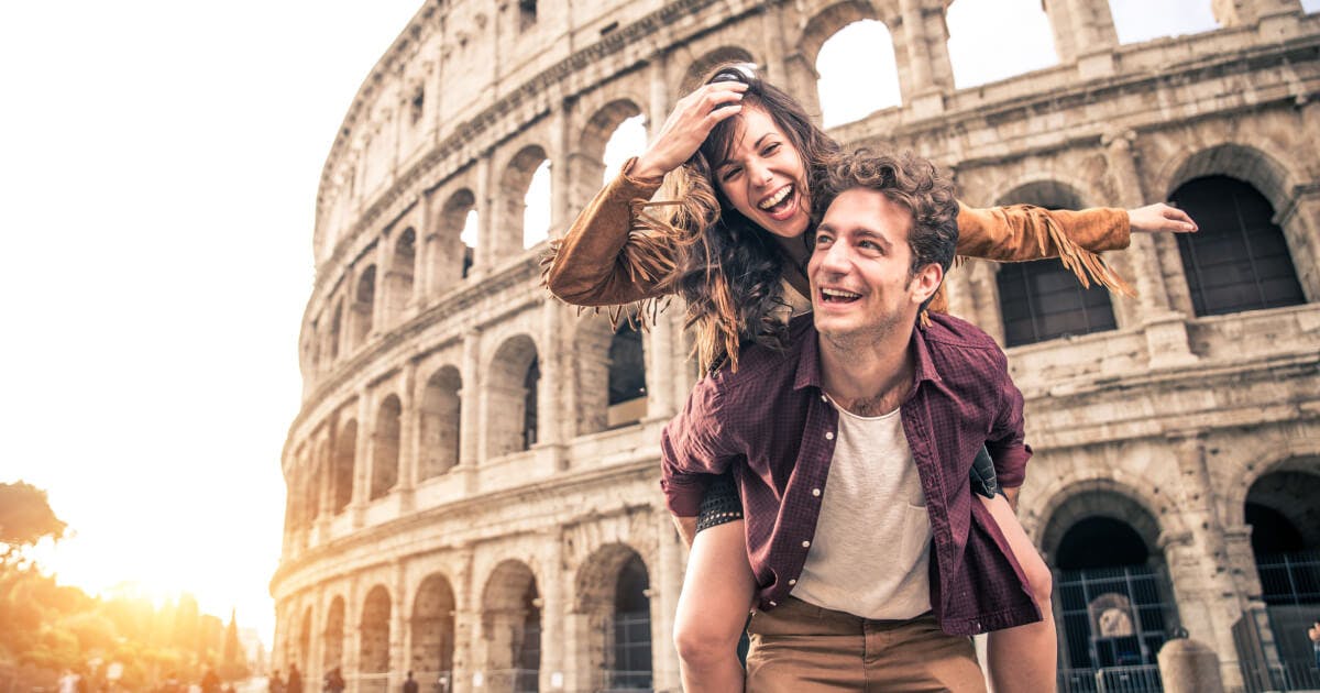 Casal se diverte em frente ao Coliseu, sorrindo e aproveitando o momento em um cenário histórico e icônico.