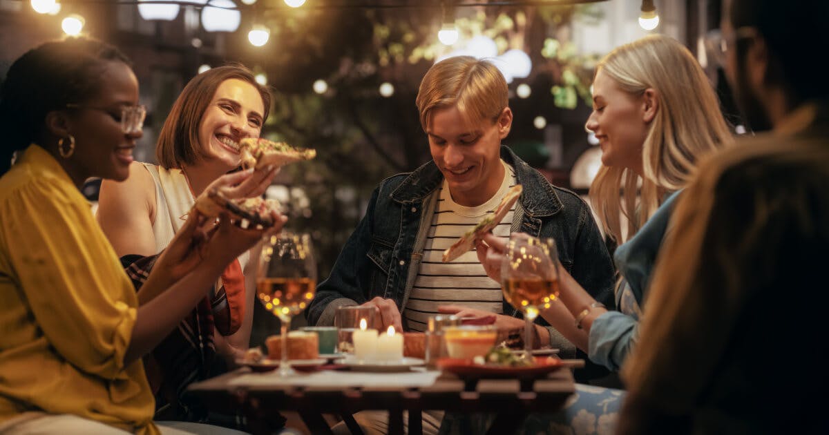 Grupo de amigos se divertindo com comida e bebidas em um restaurante ao ar livre.